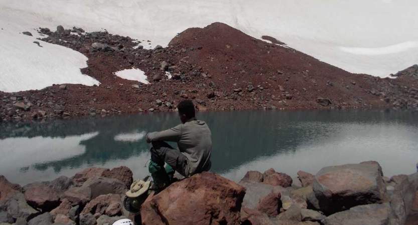 a student sits on a rock beside an alpine lake, reflecting on their outward bound experience.